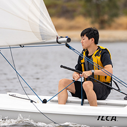 A young man in a sailboat pulling a line.